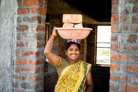 hardworking Indian smiling women with bricks on head looking at camera - concept of daily wagers...