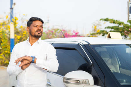 Worried indian cab driver waiting for customer in front of car - concept of cab booking service,...