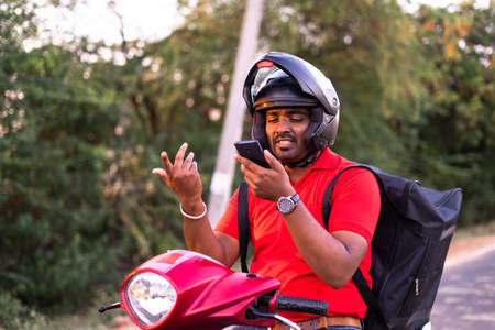 Delivery boy on scooter seraching for address by asking with customer on mobile phone - concept of deliveryman lifestyle, employment and communicationの写真素材