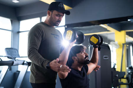focus on client, Gym trainer helping athlete to use dumbells during workout - concept of fitness training, personal coach and bodybuilding.の写真素材