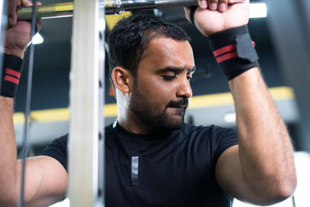 Young indian bodybuilder doing biceps workout at gym - concept of body fitness, muscle building...