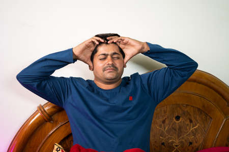 young man holding head due to headache or migraine at bedroom - concept of Healthcare,