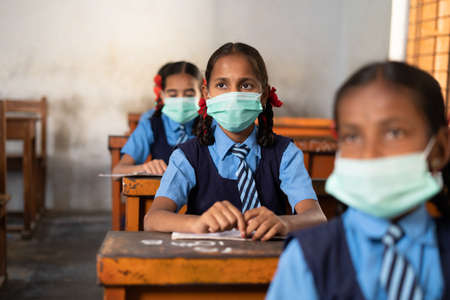 Girl kid with medical face mask listening class at school while maintaining social distance - concept of protection, pollution prevention and back to schoolの写真素材