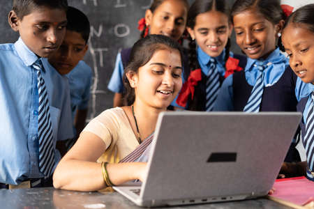 Young indian teacher teaching on laptop with school uniform students at classroom - concept of development, technology and digital educationの写真素材
