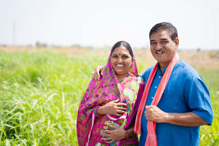 Portrait shot of smiling Indian village couple at meadow looking at camera - concept of happy family, rural lifestyle and togethernessの写真素材