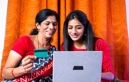 focus on daughter, Happy Indian mother and daughter busy making online payment for purchasing on laptop at home - concept of happy e-commerce shopping and secure transactionの写真素材