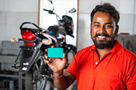 Smiling machanic showing green screen empty card by looking at camera at garage - concept of...