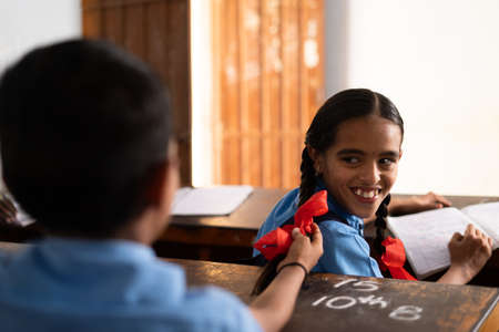Boy from behind pulling ponytail of girl at classroom - conept of childhood crush, kids mischief,...