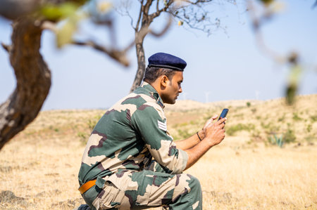 Young indian soldier uniform using mobile phone on top of mountian - concept of technology,...