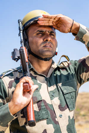 Soldier with gun hand looking around on hill top with flying indian flag in background - concpet of border protection force, serviceman on duty and securityの写真素材