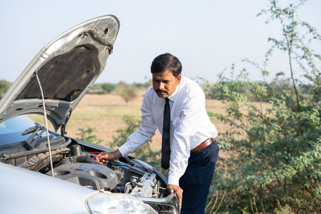 worried businessman checking broken car by lifting car hood on roadside - concept of sadness, worried, accident and problems during road tripの写真素材