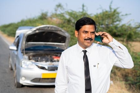 Businessman talking on mobile phone with car mechanic while car breakdown at highway road - concept of communication, car repair service and relaxation.の写真素材