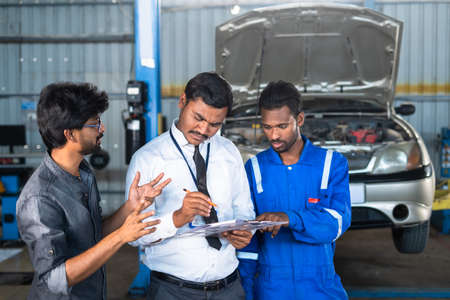 Customer discussing with Mechanic and garage executive about car problems during repair or maintenance service - concept of customer communication and employee conversationの写真素材