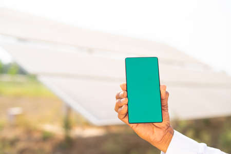 close up of farmer hands showing green screen mobile phone while standing in front of solar panel at...