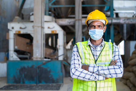 confident Industrial worker standing with medical face mask crossed arms by looking at camera at...