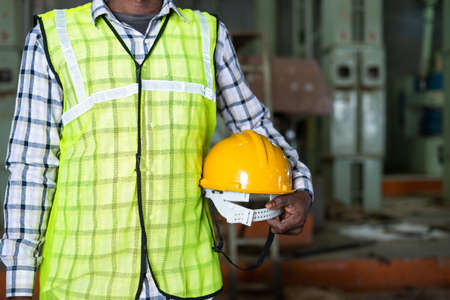 Close up shot of industrial worker standing by holding safety helmet at factory - concept of work ware, safety measures and blue collar job.の写真素材