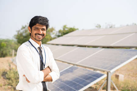 Smiling bank officer standing with crossed arms by looking at camera in front of solar panels - concept of successful, renewable energy and investment support for solar installation.の写真素材