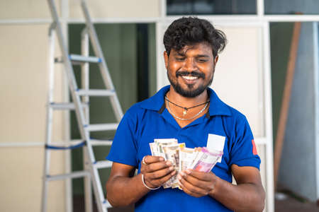 Smiling aluminium worker counting indian money at workplace - concept of banking support, earning or...