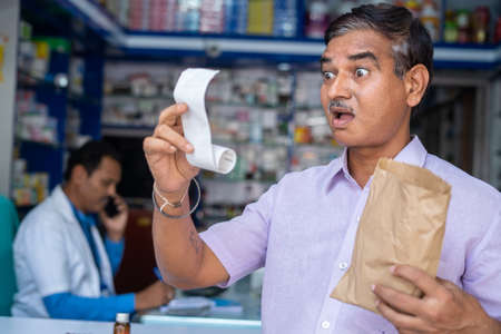 Shocked customer by seeing medicine bill while at pharmacy or medical shop - concept of increased...