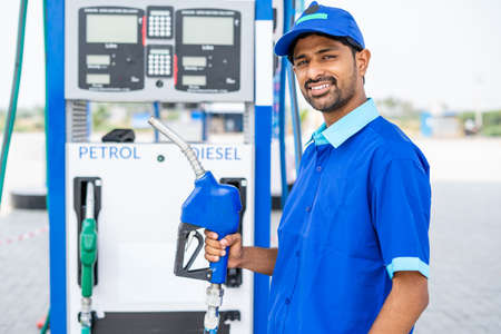 Happy petrol pump worker standing by holding fuel nozzle while looking camera at gas filling station - concept of happiness, job and petroleum service.の写真素材