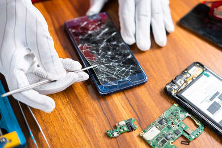 close up shot of technician removing or fixing broken mobile phone display at workshop - concept of skilled worker, professional occupation and small business.の写真素材