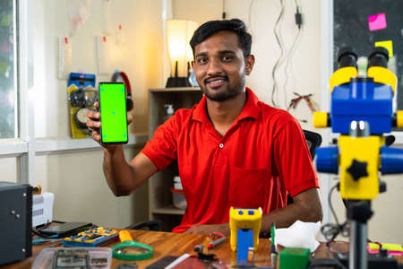 happy repairman showing green screen mobile phone by looking camera at shop - concept of online repair booking service, app promotion and advertisementの写真素材