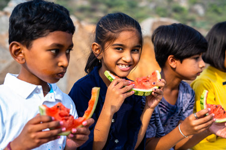 girl kid looking camera while group of kids busy eating watermelon during hot summer day - concept of dehydration, healthy eating and friendshipの写真素材