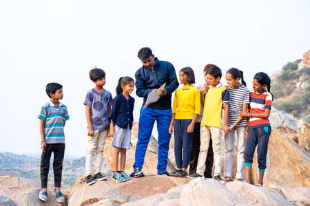 teacher explaining kids by looking map at hilltop during summer camp about location- concept of journey, togetherness, exploration and adventureの写真素材