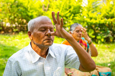 Close up shot of senior man doing nostril breathing exercise during morning at park - concept of healthy lifestyle, exercising and wellnessの写真素材