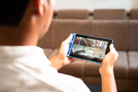 Shoulder shot of home owner checking cctv camera footage on smart digital tablet at home - concept...