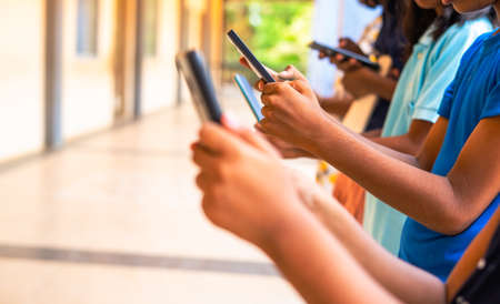 Close up shot, group of children hands busy using smartphone at school corridor - concept of social media, playing games, technology and educationの写真素材