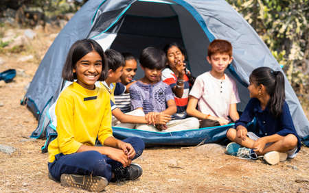 girl kid looking at camera while talking with friends at cmaping tent during summer vacation -...