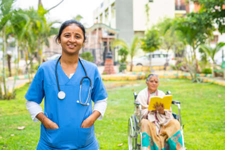 happy smiling doctor confidently standing in front of senior patient on wheelchair by looking at camera - concept of caretaker, professional occupation, medicare and treatmentの写真素材