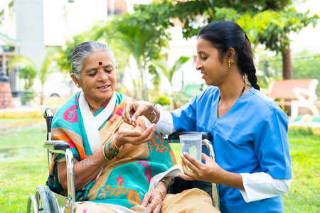 Nurse giving tablets or pills to senior woman on wheelchair with disability - concept of medicare, caretaker and treatmentの写真素材
