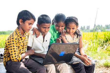 group of village kids busy using laptop near paddy field - conept of online education, technology and learning.の写真素材