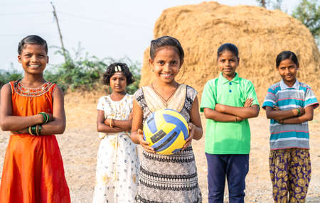 group of Indian village girls with one child holding football by looking at camera during training - concept of positiv emotion, training and hobbiesの写真素材