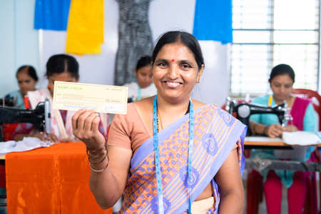 Happy women showing check by looking at camera at textile factory - concept of financial, starting...