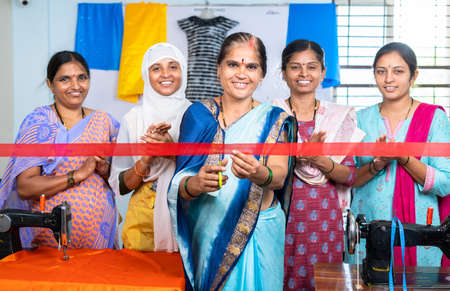 Indian woman starting new garments or tailoring small business by ribbon cutting while workers...