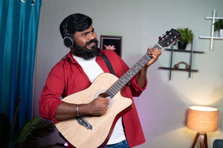 happy young beard musician enojoying by playing guitar at home - concept of hobby, weekend...