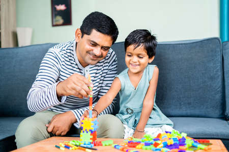 Father helping little daughter to make or build toy at home - concept of spending family time,...
