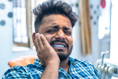 Close shot of young man suffering from toothache during dentist visit at hospital - concept of cavity, healthcare and sensitivity.の写真素材