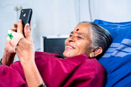 happy smiling sick woman using mobile phone at hospital while sleeping on bed - concept of technology, social media, treatment and healthcareの写真素材