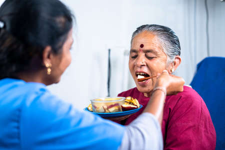 Nurse helping sick senior women to eat fruits at hospital - concept of healthcare, medicare and caretakerの写真素材