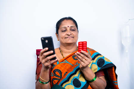 Senior women checking pills while ordering online medicines on mobile phone at home - concept of E pharmacy, technology and healthcareの写真素材