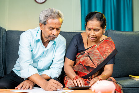 Senior couple busy calculating budget and spending of bills at home on sofa - concpet of money...