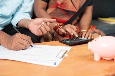 Close up shot of Senior couple hands calculating expenses or monthly bills at home with piggy bank -...