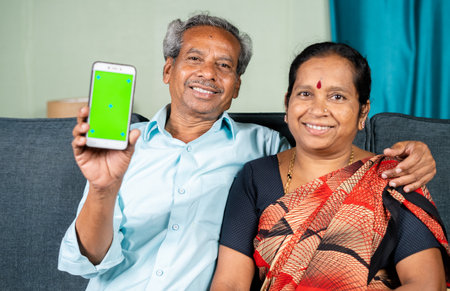 Happy smiling senior couple showing green screen mobile phone by looking at camera - concept of technology, application and togethernessの写真素材