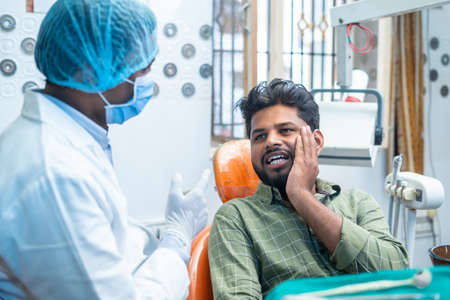 suffering young man explaining about toothache or cavity to dentist at hospital - concept of conversation, oral treatment and hygienistの写真素材