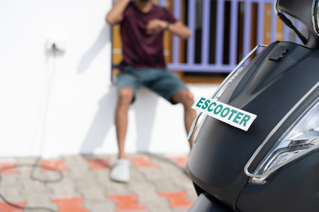 Young Man waiting for ev or electric scooter battery to charge near home at - concept of delayed charging or problems , battery issues.の写真素材