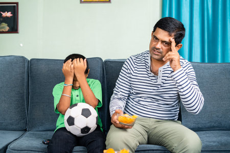 father and son got sad while live football game at home on sofa - concept of entertainment, depressed and supportersの写真素材